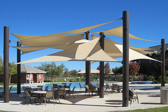 Large shade structure installation over a patio area next to a large swimming pool, providing shade.